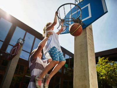 Ein Mädchen wird zum Basketballkorb hochgehoben