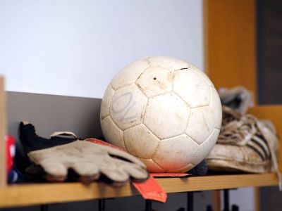 Ein Fußball, Handschuhe und Schuhe liegen in einem Regal