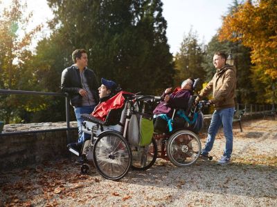 Rollstuhlfahrer sind mit Betreuern im Park unterwegs